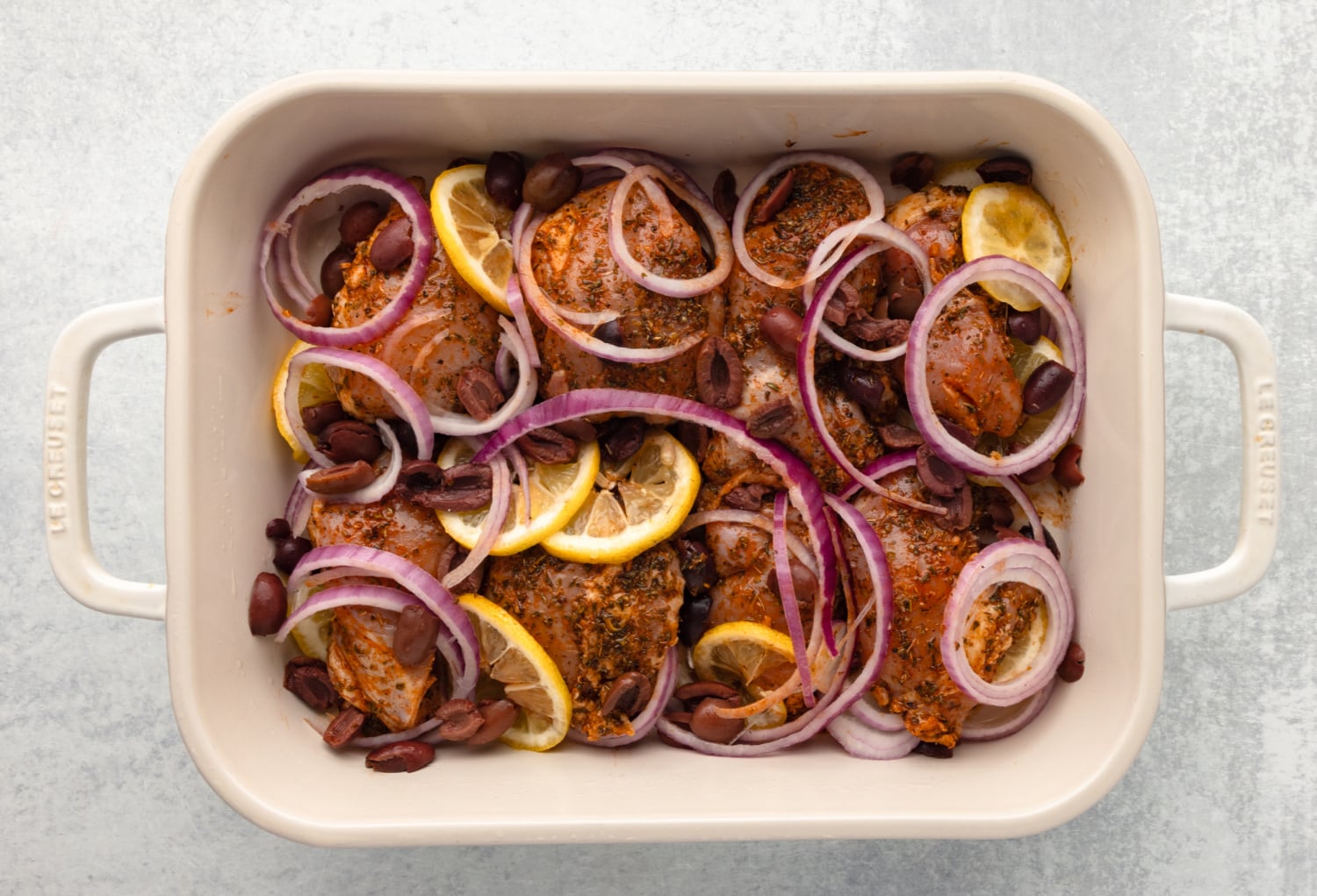 lemon slices, kalamata olives, and red onion added to baking dish with chicken