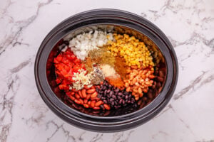 onion, garlic, tomato sauce, black beans, kidney beans, pinto beans, diced tomatoes and green chilies, frozen corn, chili powder, cumin, smoked paprika, garlic powder, oregano, coriander, cinnamon, allspice, salt, and pepper added to slow cooker