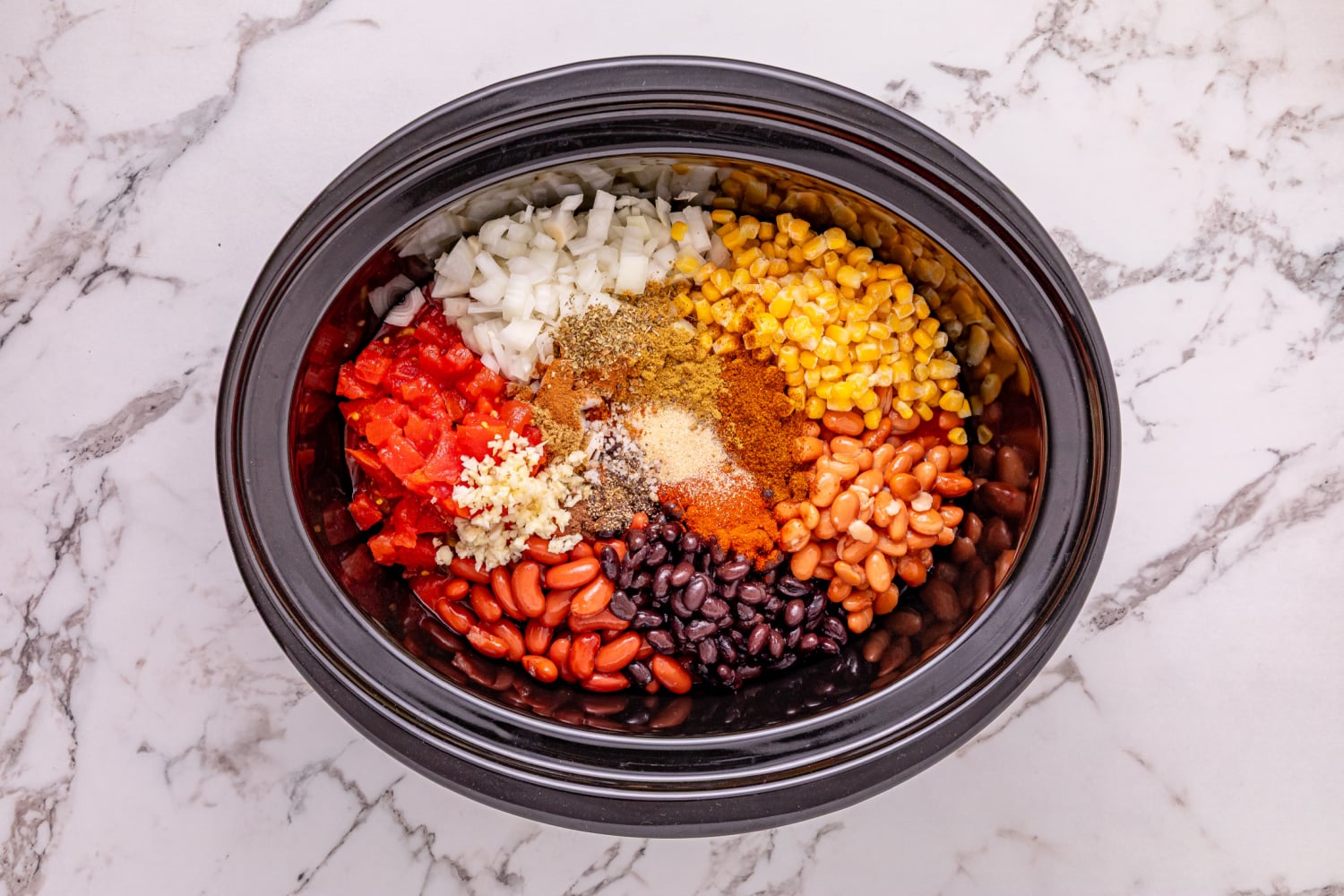onion, garlic, tomato sauce, black beans, kidney beans, pinto beans, diced tomatoes and green chilies, frozen corn, chili powder, cumin, smoked paprika, garlic powder, oregano, coriander, cinnamon, allspice, salt, and pepper added to slow cooker