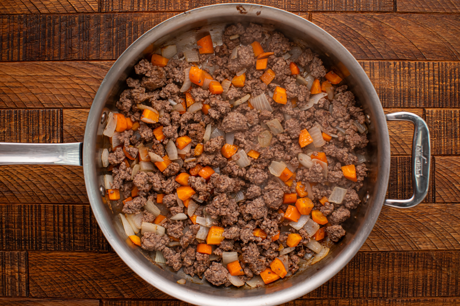 ground beef, chopped onion, and diced carrots in a pan